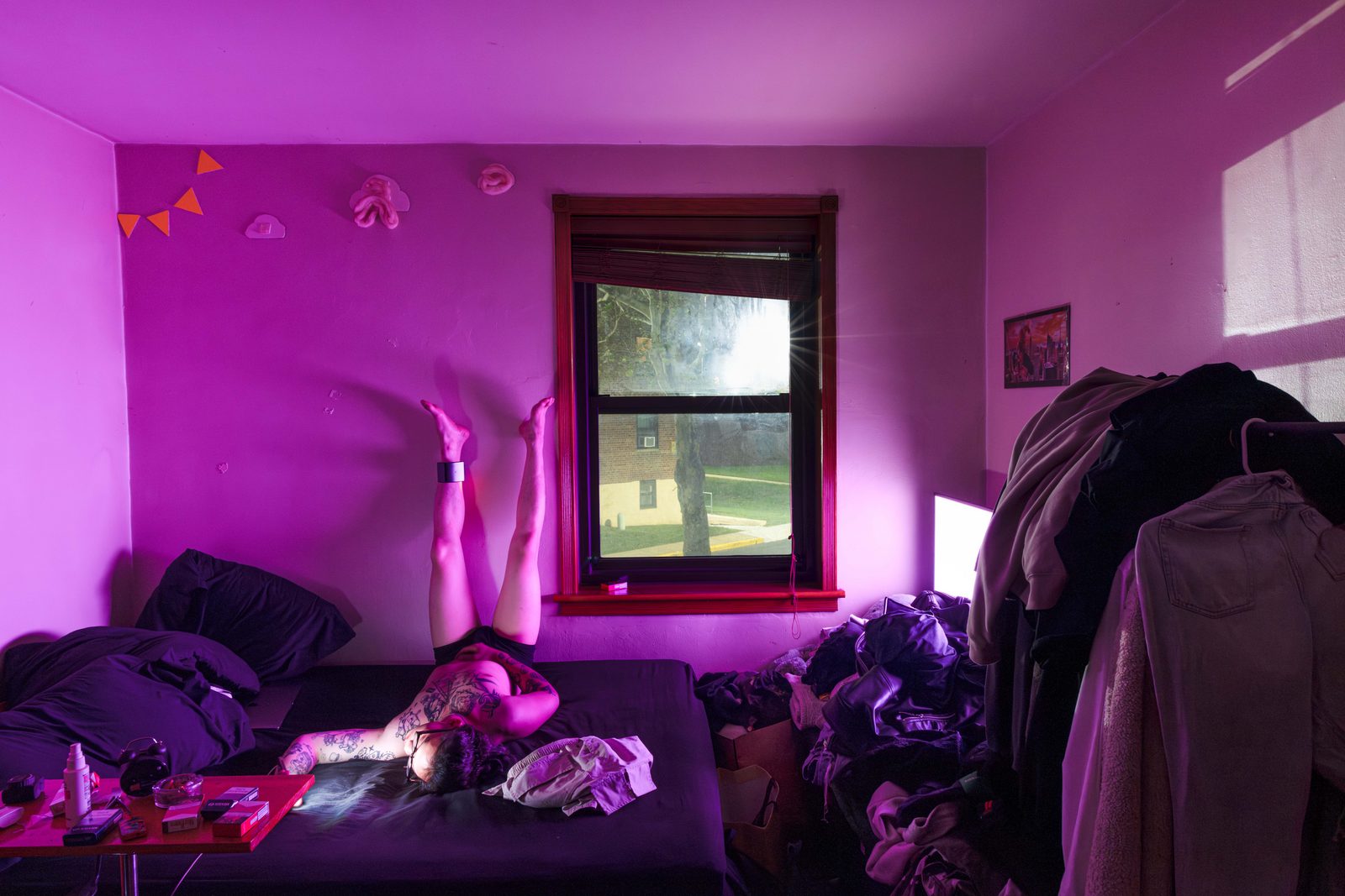 A bedroom washed in magenta light, unmade beds and clothes piled beneath a dark window — Win or Lose