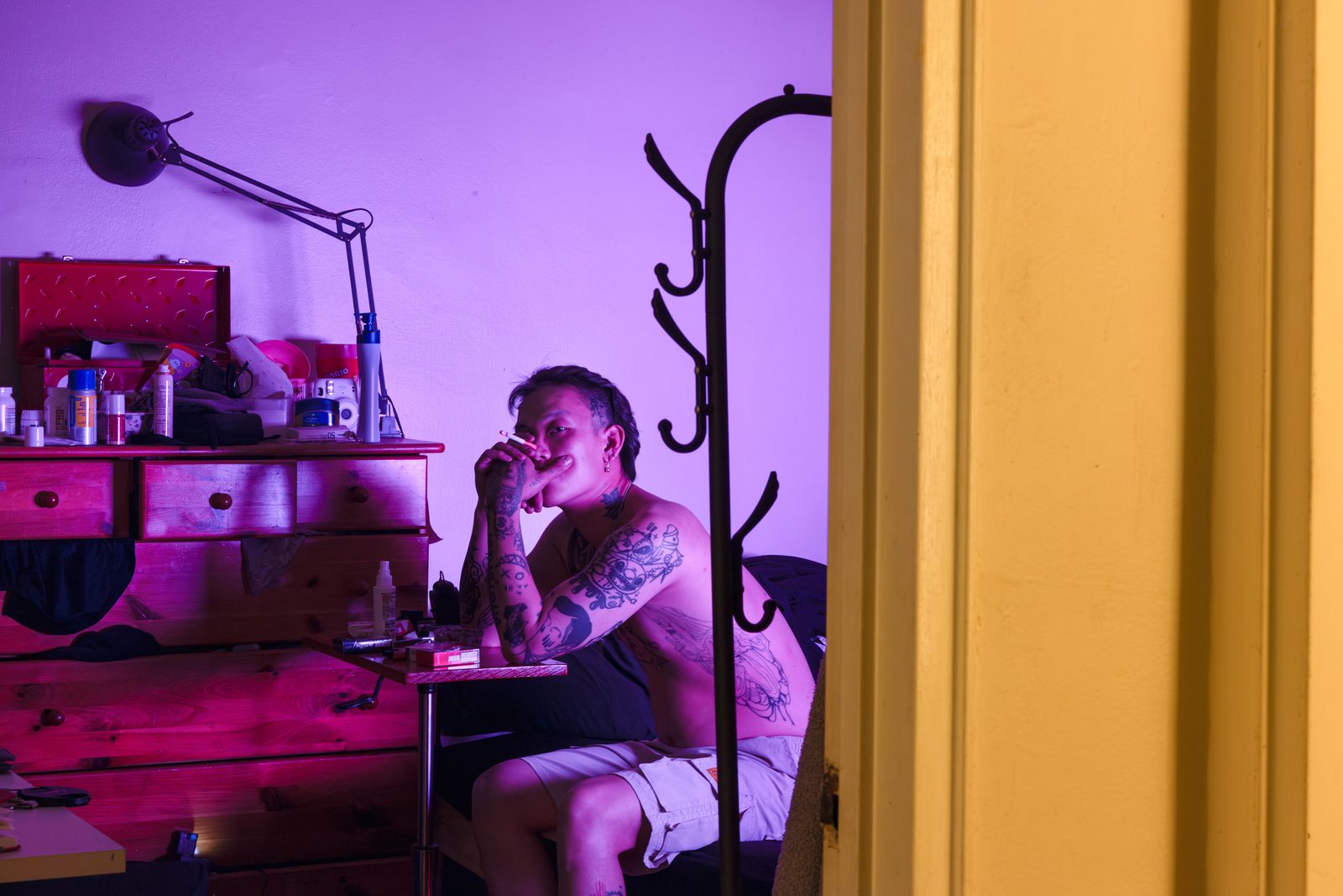 Seen through a doorway, a man sits in a cluttered room lit in purple and red — Win or Lose