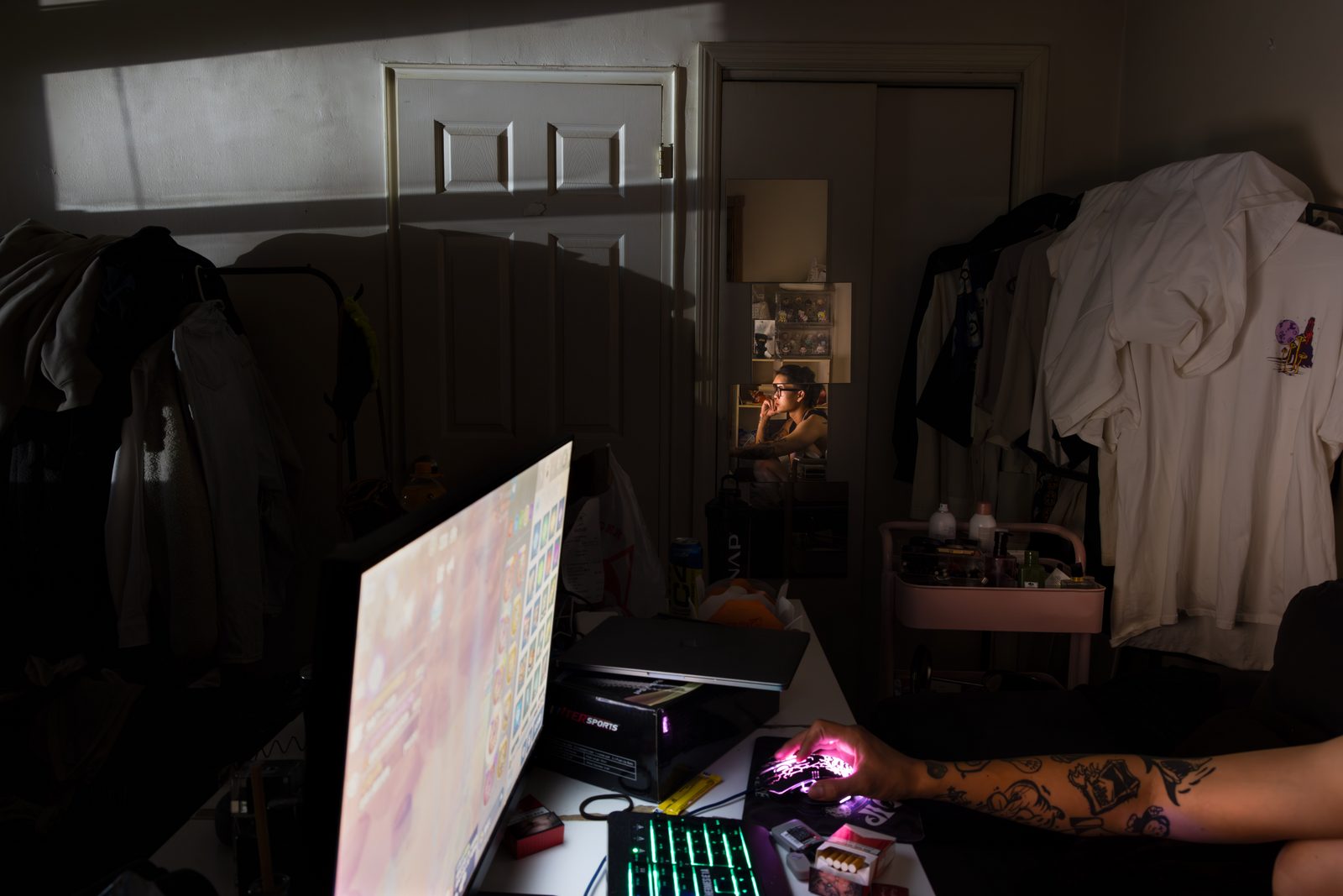 A dim room, a figure at a desk beneath a glowing screen, clothes hanging above — Win or Lose