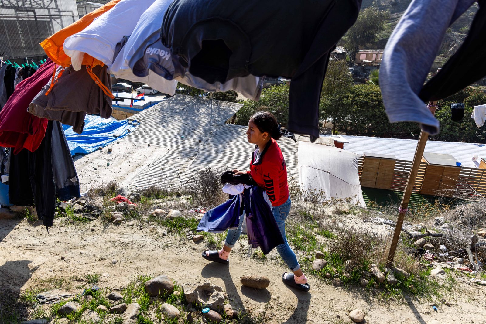 A child in a red jacket walks past makeshift shelters of tarps and blankets — The Liminal Innocence