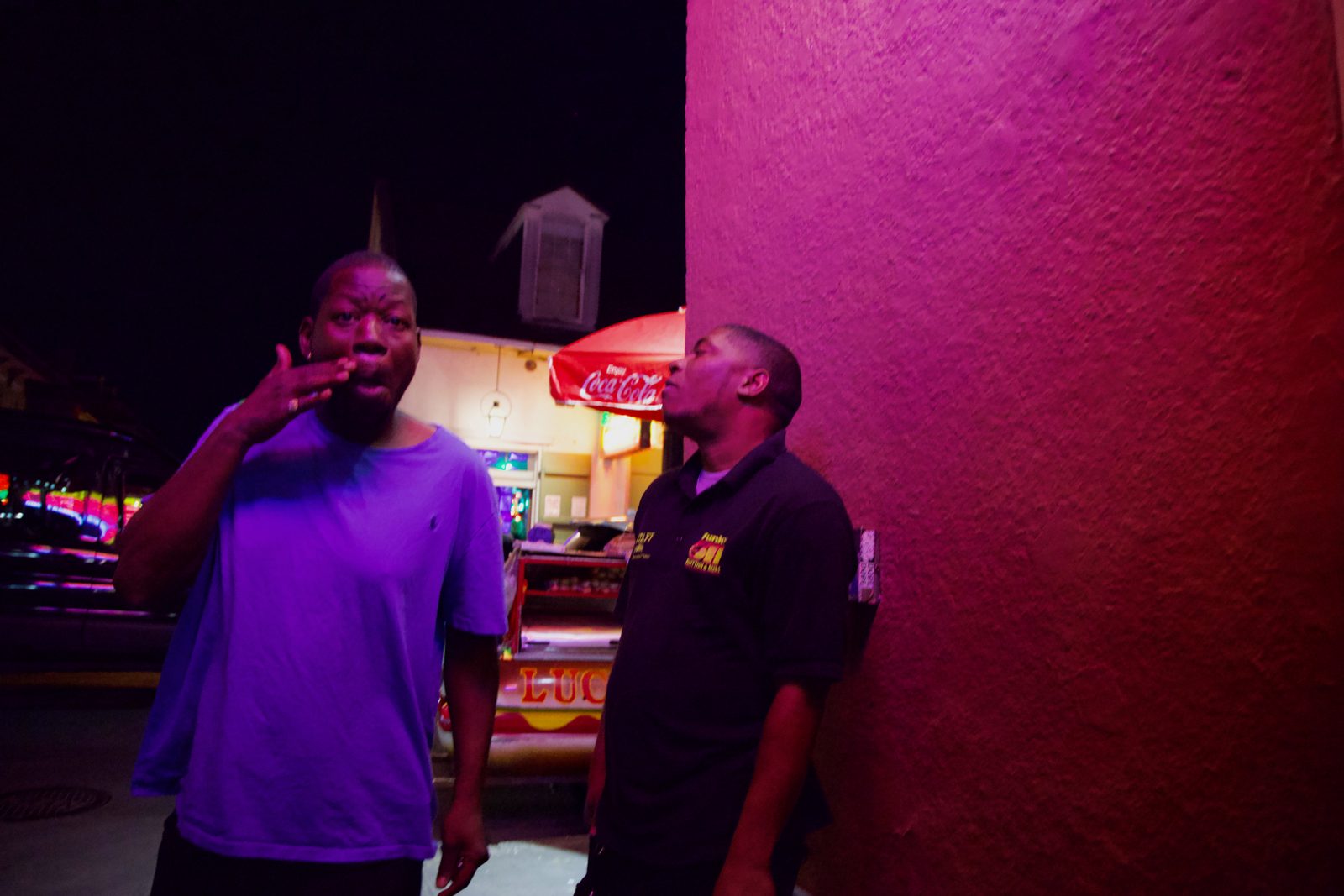 A man in a purple shirt against a magenta-lit wall at night — New Orleans