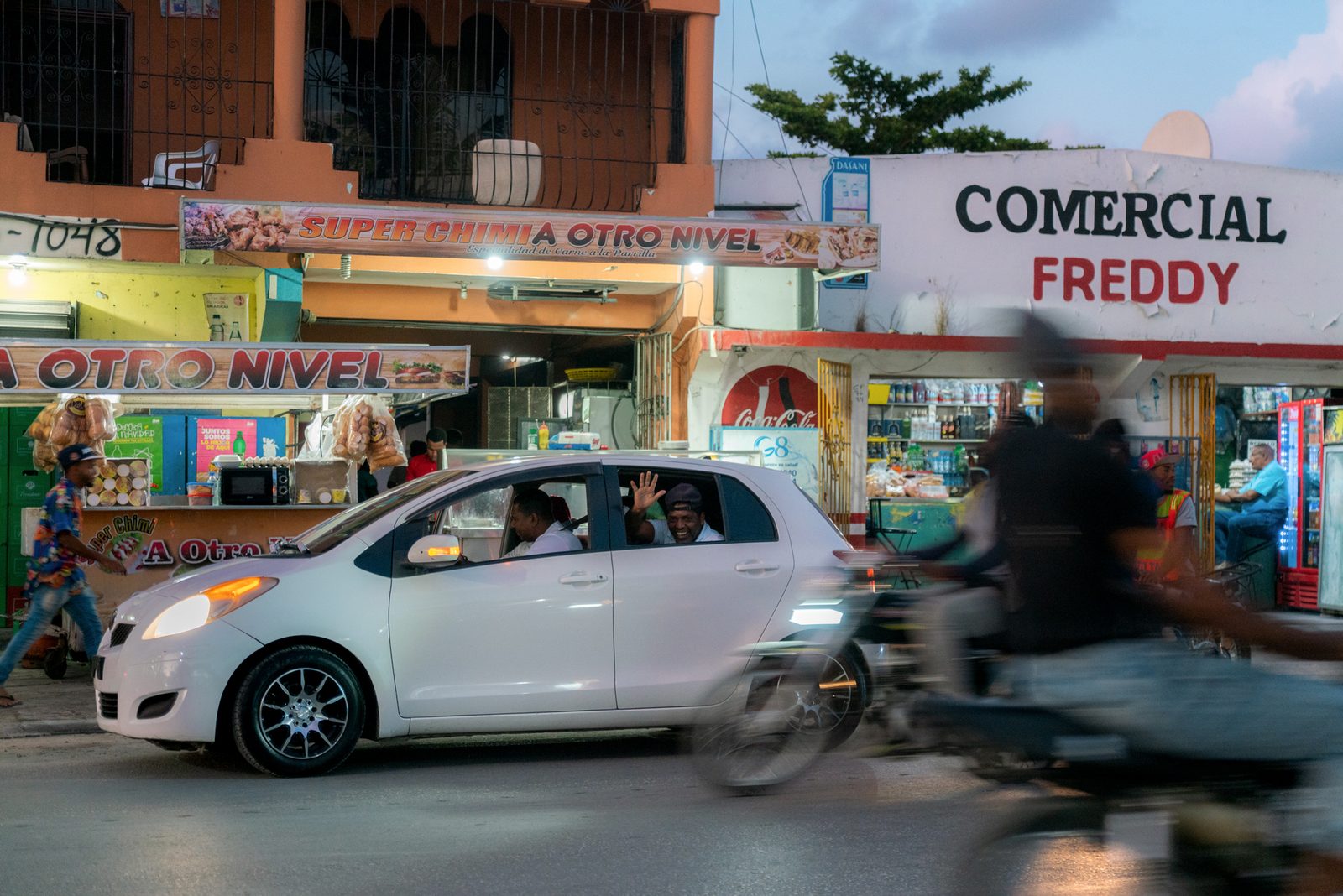 A white car parked on a street of small shops — Punta Cana